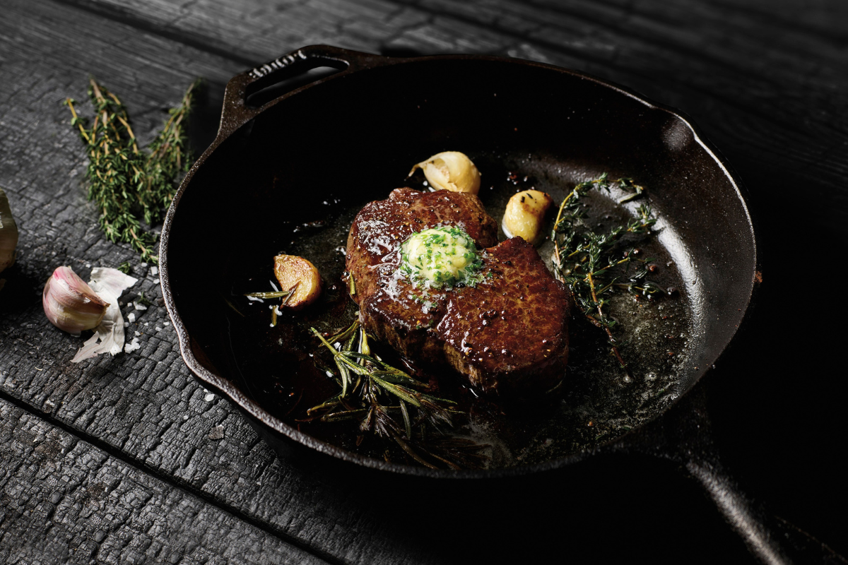 Two filet mignon steaks basted with butter and herbs in a cast iron skillet on a wooden table