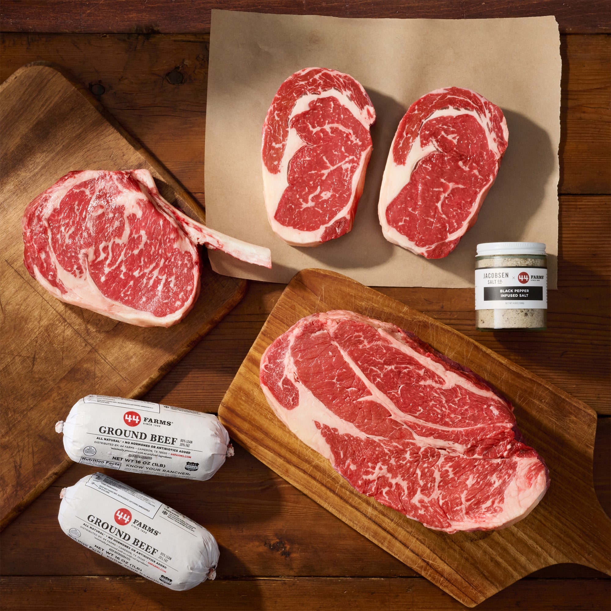 Raw beef steaks and ground beef packages on a wooden surface with a jar of seasoning.